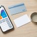 Bureau avec smartphone affichant une interface abstraite, calculatrice, carte vierge et loupe pour symboliser la vérification des prix et des frais d’un abonnement.